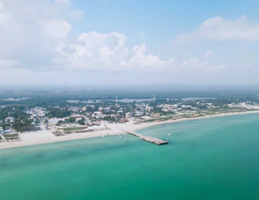 Aerial view of a coastal town with turquoise ocean, sandy beach, and a pier extending into the water
